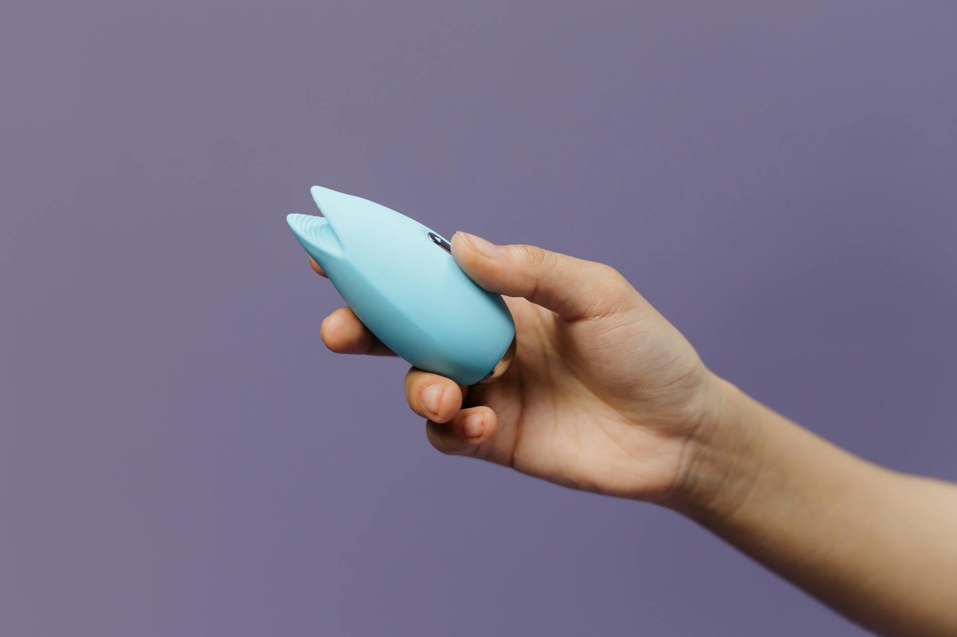 A blue silicone vibrator held in hand against a solid purple background